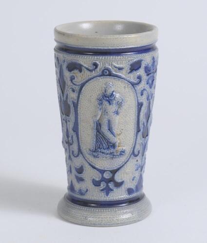 Westerwald stoneware cricket beaker, moulded in relief with three cameo panels of a batsman, after W.G. Grace, in different poses. The body highly decorated with vine and sprig decoration in cobalt blue on a grey background, with the figures highlighted i