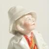 &lsquo;The Boss&rsquo;. Kinsella porcelain caricature spill vase of a young boy dressed as an Umpire in white coat wearing a white floppy hat. Printed title below spill vase. &lsquo;Copyright 482317&rsquo; to base. German, circa early 1900&rsquo;s. Approximately 5.5&rdquo; tall. Damage with - 5