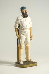 &lsquo;W.G. Grace&rsquo;?. Large modern figure of a bearded batsman wearing a blue and red hooped cap with bat and gloves in hands. The figure stands on grass base and signed &lsquo;Peter Mook 98&rsquo;. Approx 14.5&rdquo; tall. VG