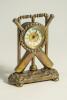 Cricket clock. A Victorian brass mantel clock. The case in the form of a set of stumps with crossed bats and ball on an oval naturalistic case base with bun feet. Dial with gilded centre. Approximately 6.5&rdquo; high by 5&rdquo; wide. British Union Clock Company sta