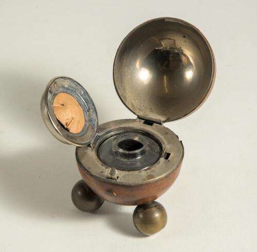 Cricket ball inkwell. Leather cricket ball ink well, well made with seam and stitched quarters. The ball, mounted on three ball feet, is split and hinged and opens to reveal a silver metal liner with an original glass ink well. Approximately 2.75&rdquo; circumf