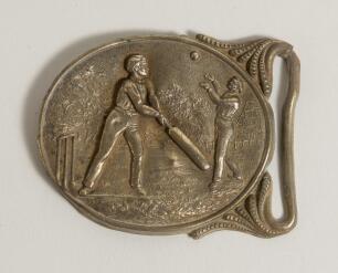 Cricket belt buckle. A large oval shaped belt buckle in brass featuring a cricket match in progress with batsman at the wicket striking the ball, a fielder is about to catch him out, a house and trees to background. Circa 1870. Approximately 3.25&rdquo;x2.5&rdquo;. T
