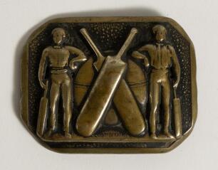 Cricket belt buckle. An oblong shaped brass belt buckle with cricket ball and crossed bats to centre, a cricketer either side appear to be leaning on the ball and holding bats . Circa 1870. Approximately 2.5&rdquo;x2&rdquo;. Good condition