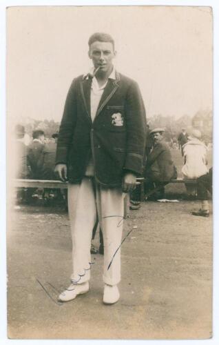 Maurice William Tate. Sussex & England 1912-1937. Sepia real photograph postcard of Tate standing full length wearing cricket attire and M.C.C. touring blazer, pipe in mouth, spectators in the background. Signed to the photograph &lsquo;Maurice Tate&rsquo;. Publisher
