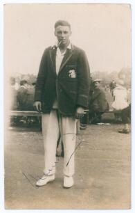 Maurice William Tate. Sussex & England 1912-1937. Sepia real photograph postcard of Tate standing full length wearing cricket attire and M.C.C. touring blazer, pipe in mouth, spectators in the background. Signed to the photograph &lsquo;Maurice Tate&rsquo;. Publisher