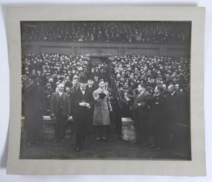 King George VI 1930s. A large original mono photograph of King George VI entering the field of an unknown sports stadium from a grandstand accompanied by dignitaries wearing formal attire and bowler hats. In the stands, large crowds are looking on enthusi