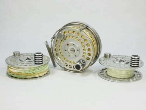 An Ari't Hart Tweed salmon fly reel and two spare spools, right hand wind model with brushed steel finish, counter-balanced handle, full annular wire line guide, stancheon foot, multi-perforated drum and rear plate with six large ventilation ports, rear 