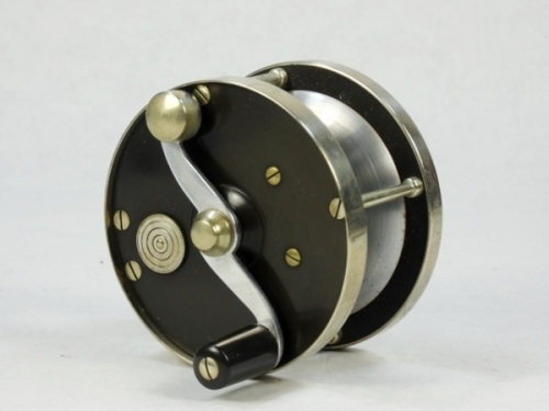 A scarce Otto Zwarg Saguenay 1/0 direct drive light salmon fly reel and block leather case, ebonite and nickel silver construction, tapered ebonite handle on serpentine crank winding arm set within an anti-foul rim, pieced alloy foot stamped model details