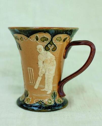 Doulton Lambeth stoneware mug with flared lip in art nouveau style, with three moulded relief vignettes of cricketers, a batsman, bowler and wicket keeper, Abel, Woods and McGregor in white on a brown background, with floral leaf decoration above and belo