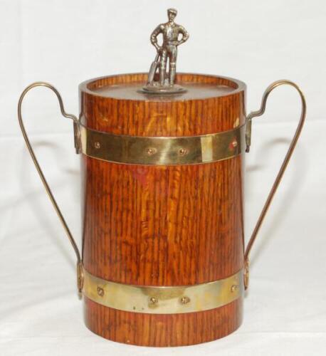 Cricket ice bucket. Wooden two handled metal lined ice bucket. The wooden ice bucket with brass bands similar to a barrel with brass handles. The wooden lid with metal cricketer batsman finial, wearing cap, with bat to side to top. Overall 9.5" tall. Date