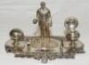 Lawn bowls. Silver metal (EPNS) ink stand of a 'bowler' standing holding a ball with three more balls at his feet. To either side, two inkwells in the form of bowling balls, one with glass liner, and foliage decoration. Maker's mark to underside for 'J.D.