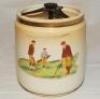 Golf tobacco jar. Carlton Ware jar with removable cover c.1910s/1920s. To one side a colour transfer image of two gentlemen playing golf with a caddy, to the reverse, a crossed clubs emblem with golf ball and scroll inscribed 'Far and Sure'. 5" tall. Carl