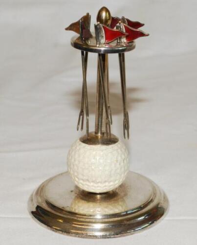 Golf. Silver metal EPNS cocktail stick holder comprising six pronged golf flags with red enamel decoration, suspended from a top set on a golf ball, in turn set on circular metal base. Maker's mark P.H.V. & Co. to base. 5.5" tall. Some crazing to the golf