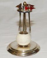 Golf. Silver metal EPNS cocktail stick holder comprising six pronged golf flags with red enamel decoration, suspended from a top set on a golf ball, in turn set on circular metal base. Maker's mark P.H.V. & Co. to base. 5.5" tall. Some crazing to the golf