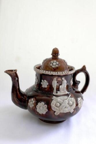 Measham Ware cricket teapot. A Victorian saltglaze stoneware brown teapot with lid. The teapot with sprigged decoration in white of two cricket figures, believed to be Pilch and Box to each side, below the figures are sprigged crossed bat and stumps with 