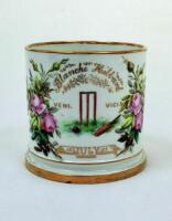 Cricket mug/cup. A white ceramic mug with central image of a cricket wicket, bat and ball with inscription above and below 'Blanche Hibbard. Veni Vici July 1879'. This floral rose design to borders. Gold lustre to base, rim and handle. The mug stands 3.25