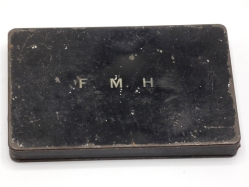 A black japanned rectangular fly box, lid white painted “F.M.H.", cream painted interior fitted eight rows of fine wire spring locking fly holders on five raised metal bars, holding a selection of thirty of F.M.H.’s own trout flies, various patterns, pai
