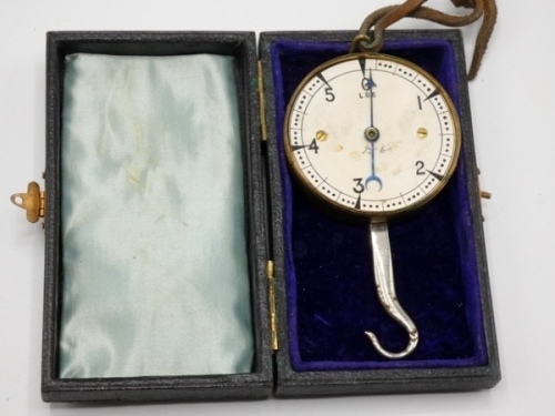 F.M.H.’s brass spring balance fish scale, contained in original velvet and silk lined rectangular black rexine case and with circular brass cased paper dial ink detailed 0-5lbs graduations, blued steel arrow indicator, steel hook and brass loop eye, circ