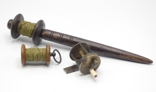 A 19th Century fruitwood thumb reel of turned bobbing construction, one end with circular brass plate mounted thumb ring, crack to one end plate, a fruitwood bank runner, the turned bobbin mounted on tapered spike handle with three bands of concentric cut