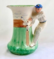 Burleigh Ware art deco ceramic cricket jug c1930's. The jug with cricket field and pavilion design to body with moulded batsman handle. The batsman wearing a blue cap and yellow/blue sash. The jug is 7.5" tall with 'beehive' Burleigh stamp to base. Very g