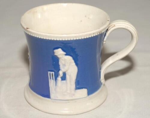 Staffordshire blue ground waisted cricket mug with strap handle and beaded rim. With three relief moulded figures of a batsman, bowler and wicket keeper in cream, believed to be Lillywhite, Pilch and Box. c1860. Two minor chips to rim otherwise in good co