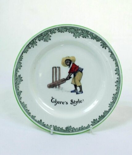 'There's Style'. A Royal Doulton Black Boy dessert plate, entitled 'There's Style' printed with a boy in a white shirt, red waistcoat, yellow trousers and a floppy hat taking guard in front of the stumps with bat almost horizontal. Green floral decoration