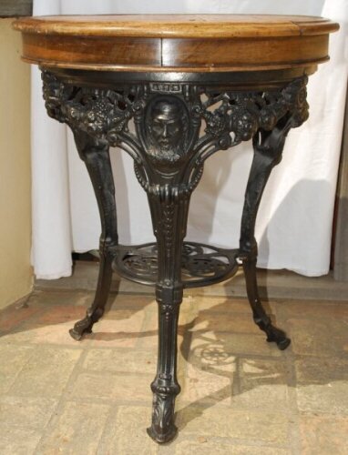 W.G. Grace. Original cast iron circular public house table with circular wooden top, supported by three leg moulded with portrait busts of Grace, with imprinted initials 'W.G' above, wearing cricket cap to top of each leg with decorated pierced apron of b