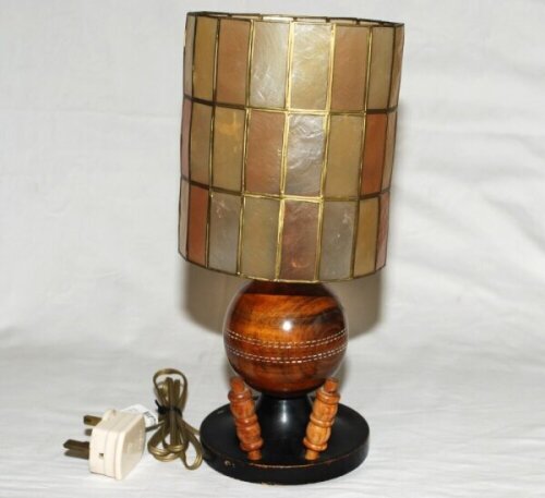 Cricket table lamp in the form of a wooden cricket ball mounted on circular base with two bails, with drum shade in the style of Tiffany. Overall 13" tall. Good condition. Sold with a selection of ceramics and metalware including a groundsman's cricketer'