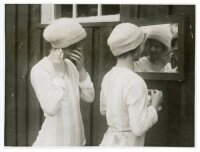 'Girl Footballers in Training for Their Cup' c.1930s. Original mono press photograph of two members of the Bramtoco (Southampton) ladies football team, both wearing woollen hats, preparing themselves in front of a mirror before a match. The press caption 