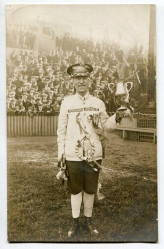 Tottenham Hotspur F.A. Cup Win. Season 1920/1921...?. Mono real photograph postcard of what appears to be a moustached fan, standing on the pitch with crowd behind, dressed for the occasion, wearing a peaked cap with title 'Tottenham Hotspur' to front and