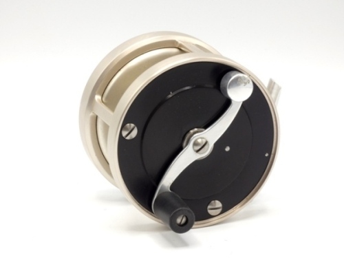 A fine and rare S.E. Bogdan model 150 multiplying salmon fly reel, left hand wind model with black and champagne anodised finish, counter-balanced serpentine scroll handle set within an anti-foul rim, alloy block foot, stamped model details, rear milled