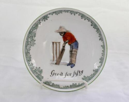 ‘Good for Fifty’ Royal Doulton Black Boy saucer, entitled ‘Good for Fifty’ printed with a boy in red shirt and a floppy hat in batting pose in front of the wicket to centre. Green floral decoration to edge. 5.5” diameter. Doulton backstamp and number ‘E43