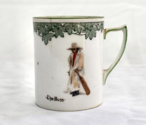 ‘The Boss’. A Royal Doulton Black Boy miniature mug, entitled ‘The Boss’ printed, to one side, printed with a boy in red shirt and a floppy hat, wearing an umpires’s coat and holding a bat to side, to verso, the crest ‘The All Black Team’. Green floral de