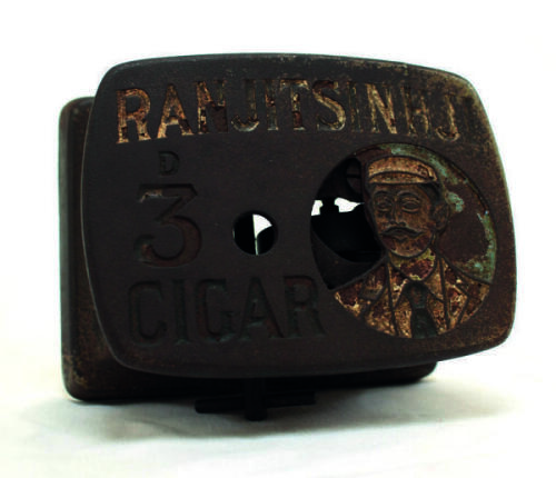 ‘Ranjitsinhji 3d Cigar’. Large heavy cast iron cigar cutter, the metal top with portrait of Ranjitsinhji, head and shoulders, wearing cap, blazer and tie with the wording ‘’Ranjitsinhji 3d Cigar’ to side. Wind-up mechanical mechanism beneath. ‘Patent numb