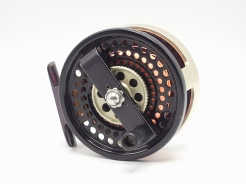 A Ted Juracsik Billy Pate Bonefish anti-reverse saltwater fly reel, black/gold anodised left hand wind model with composition handle mounted on cross-bar winding arm above a milled wheel tension adjuster, pierced block foot, light use only, in neoprene p