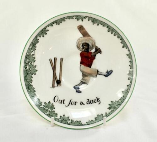 ‘Out for a Duck’ Royal Doulton Black Boy saucer, entitled ‘Out for a Duck’ printed with a boy cricketer in red shirt and a floppy hat in batting pose having attempted a big shot, looking back to see the ball hit his wicket. Green floral decoration to edge