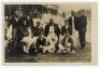 The Ashes. England v Australia 1899. Early sepia real photograph postcard of the ‘England XI’ seated and standing in rows wearing cricket attire, assorted blazers and caps. The Trent Bridge stands and pavilion in the background. Printed title and players’