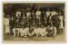 ‘Essex v Hants, Colchester 1920’. Sepia real photograph postcard of the Essex and Hampshire teams seated and standing in rows wearing cricket attire and assorted blazers and caps, in front of the pavilion. Taken at the match played at Colchester, 19th- 22