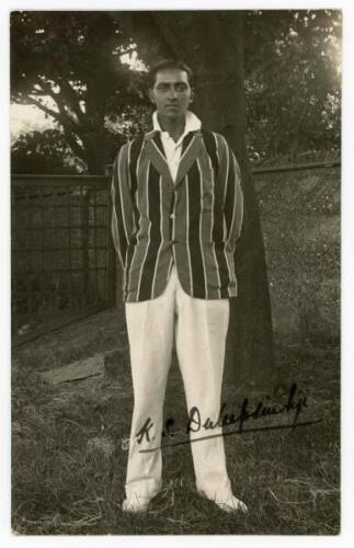 Kumar Shri Duleepsinhji. Sussex, Cambridge University & England 1924-1932. Excellent original mono real photograph postcard of Duleep standing full length under a tree, wearing cricket attire and striped blazer. The postcard very nicely signed in black in