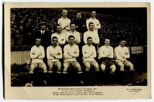 ‘Tottenham Hotspur Cup Team 1921’. Early mono real photograph postcard of the team and trainer, Minter, standing and seated in rows on the pitch with the large crowd behind them, with printed title ‘Tottenham Hotspur Cup Team 1921’ and players names print