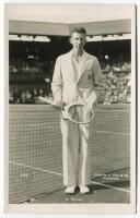 John Donald Budge. Original mono real photograph postcard of Budge, standing full length, wearing tennis attire and blazer at the net at Wimbledon and holding a racket. Players name printed to lower border. Card no. V82 in a series issued by Edwin Trim & 