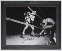 Jake LaMotta. Large mono action photograph of LaMotta knocking out his opponent, sending flying through the ropes. Signed to the photograph by LaMotta. 15.75”x11.75”. Mounted, framed and glazed, overall 19”x15”. VG.