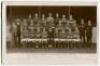 Woolwich Arsenal Football Club 1911-12’. Mono real photograph postcard of the Woolwich Arsenal team, staff and directors standing and sitting in rows in front of the stand. Title and players names printed to lower border. Postally used and dated 1911. A r