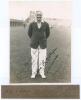 Arthur Edward Robert Gilligan. Cambridge University, Surrey, Sussex & England 1919-1932. Original sepia photograph of Gilligan depicted full length wearing cricket attire and England blazer at Scarborough with the scoreboard and grandstand in the backgrou