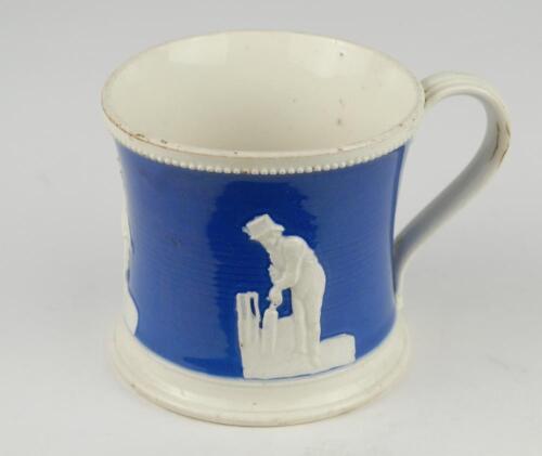 Staffordshire blue ground waisted cricket mug with strap handle and beaded rim. With three relief moulded figures of a batsman, bowler and wicket keeper in cream, believed to be Lillywhite, Pilch and Box. c1860. Very minor wear to rim, minor wear to base 