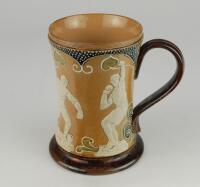 Doulton Lambeth stoneware waisted body tankard with art noveau designs of stylised hearts and white on blue dots, with sporting figures in relief in white showing two footballers with ball, athletics runner and shot putting. 6&rdquo; tall. Impressed Doulton Lam