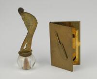 Cricket card holder. Slim brass card holder with raised cricket bat decoration to lid. Sold with a brass bottle stop, a brass figure of a batsman with wooden/cork stopper. This is placed in a circular glass upright holder for when not in use. 5.5” tall. B