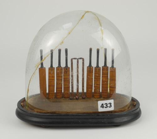 Cricket bat display. Wooden display stand with velvet lined base displaying eight miniature carved cricket bats with stringed (thread) handles, a set of stumps and bails to centre and three red cricket ball in front of the stumps. perspex dome covers the 