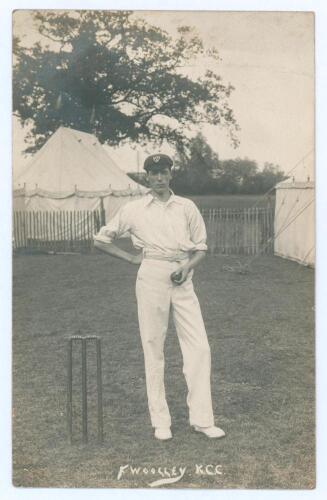 Frank Edward Woolley. Kent & England 1906-1938. Early sepia real photograph postcard of a youthful Woolley standing full length beside a wicket, wearing cricket attire and cap, with ball in hand, marquees in the background. The Alma Studio, Tonbridge. Pos