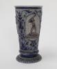 Westerwald stoneware cricket beaker, moulded in relief with three cameo panels of a batsman, after W.G. Grace, in different poses. The body decorated with vine and sprig decoration in cobalt blue on a grey background. Blue rings to rim and to foot. Approx - 2